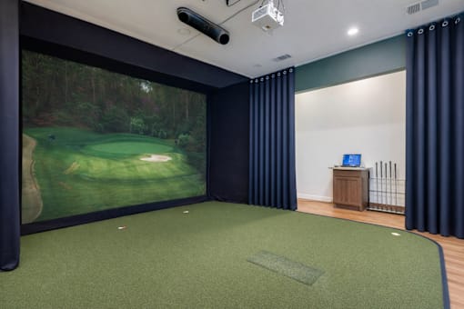 A room with a golf simulator and a green carpet.