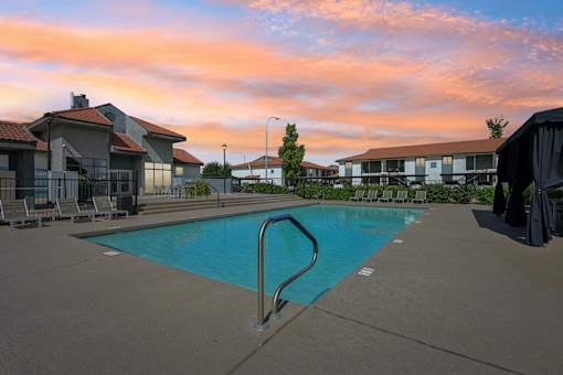A swimming pool surrounded by a concrete floor and a metal ladder.