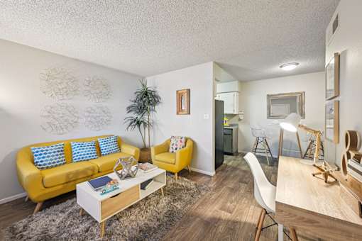 Pet-Friendly Apartments in Mesa, AZ - Mesa Station Apartments - Living Room With A Yellow Sofa, Matching Accent Chair, Coffee Table, Desk Area, and Dining Nook.