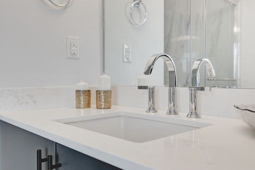 A white sink with a silver faucet and two candles on a marble counter.