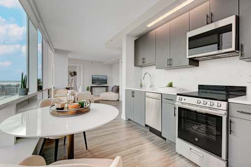 A modern kitchen with a white table and chairs, a microwave above the stove, and a view of the ocean through the window.