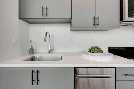 A modern kitchen with a stainless steel sink and a plate of cucumbers on the counter.