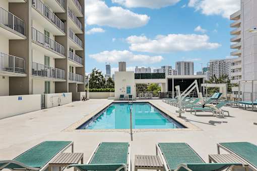 A large swimming pool surrounded by lounge chairs and apartment buildings.