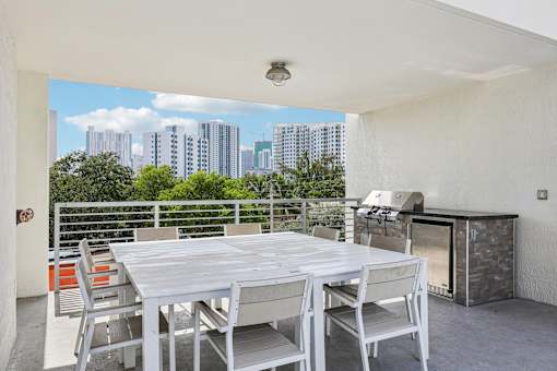 A white table and chairs are set up on a balcony with a cityscape in the background.