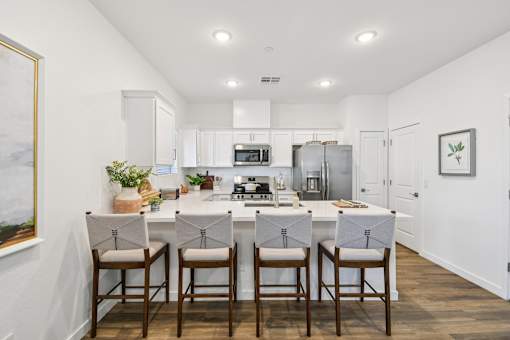 A kitchen with white cabinets and a white island with three chairs.