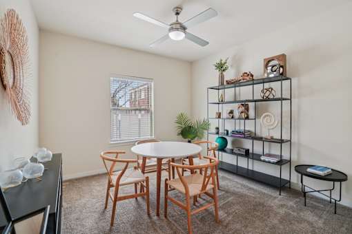 A room with a white table and chairs, a fan, and a shelf with various items.
