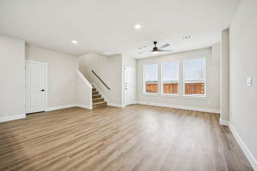 A spacious room with wooden flooring and a staircase leading to the upper level.