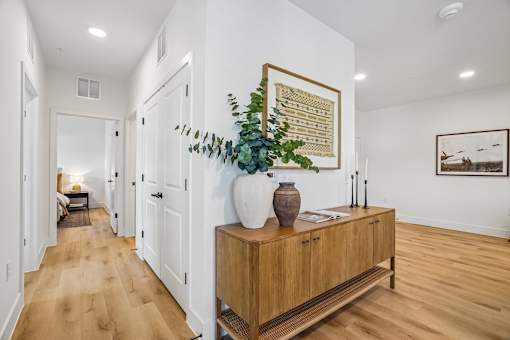 A long hallway with a wooden floor and a vase on a cabinet.