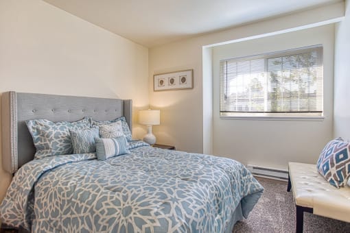 1, 2, 3 BR Apartments in Puyallup, WA - One Canyon Place - Bedroom with King-Sized Bed, Ottoman, Wall-to-Wall Carpeting, Window with Blinds, and Nightstand