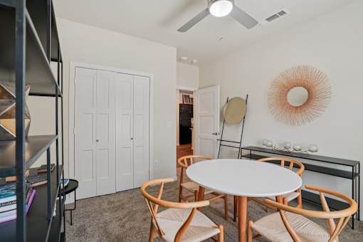A white dining table with four chairs and a shelf with books and decorative items.