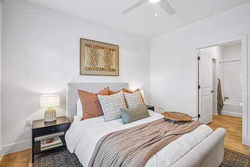 A bedroom with a bed, pillows, a ceiling fan, and a painting on the wall.