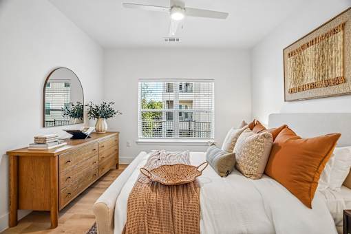A bedroom with a bed, dresser, mirror, and window.