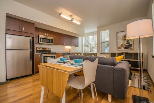 Apartments in Portland, OR - Corbett Heights - Dining Area with Hardwood-Style Floor, Folding Table, Chairs, Floor Lamp, and View of Living Area and Kitchen.