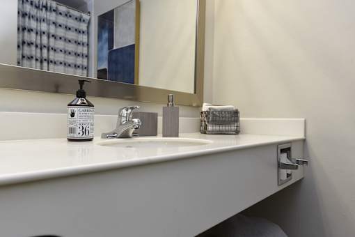 A white sink with a soap dispenser and a mirror above it.