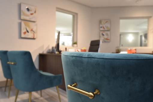A blue chair with a gold handle is in the foreground of a room with a desk and a mirror.