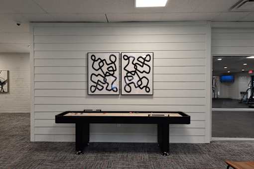 A black pool table in a room with a white wall and a painting above it.