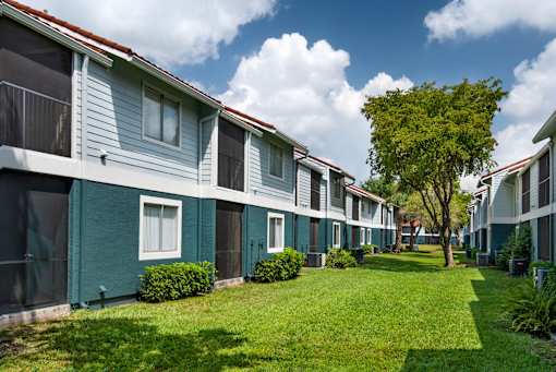 A row of houses with green lawns and trees in front.