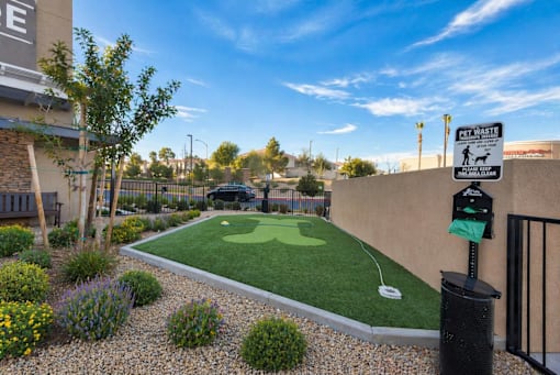 A small putting green is surrounded by a low fence and a sign that says "Pet Waste.".
