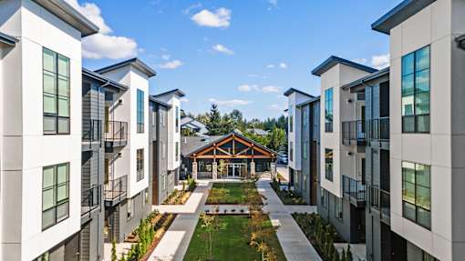 A modern apartment complex with a central courtyard and a wooden building in the background.