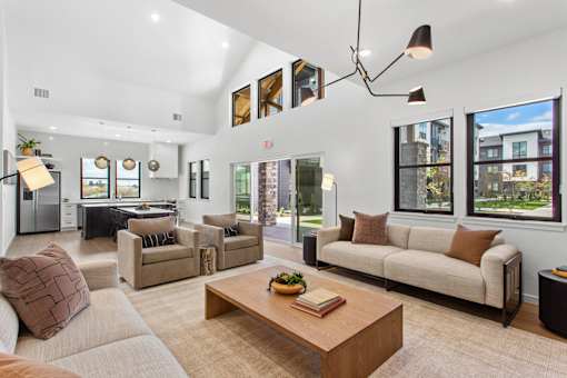 A modern living room with a large couch, a coffee table, and a kitchen area in the background.