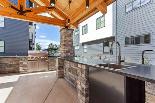 A modern outdoor kitchen with a wooden pergola and a stone wall.