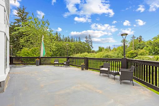 A patio with chairs and a table is surrounded by trees.