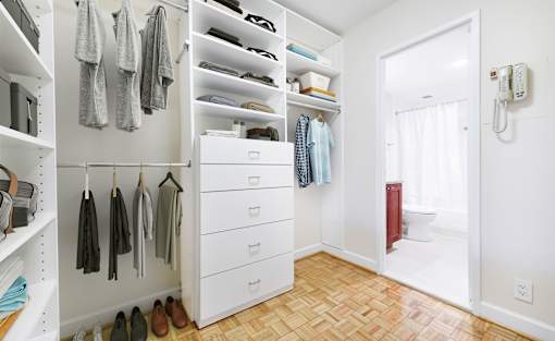A white closet with clothes hanging and shoes on the floor.