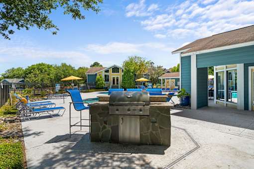 A sunny day at the poolside with a stone grill and chairs.