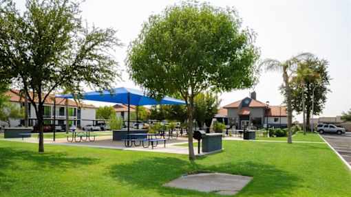 a park with tables and umbrellas and houses in the background