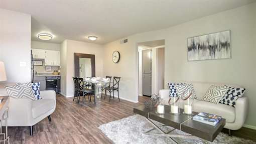 Apartments in Mesa, AZ, for Rent - Mesa Station - Open Concept Living Room with Wood-Style Flooring, Decorative Rug, Coffee Table, Couch, Chair with Decorative Pillows, and Access to the Dining Area and Kitchen.