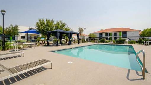 Mesa, AZ, Apartments with In-Unit Washer and Dryer - Mesa Station - Swimming Pool with Gazebo, Tanning Lounge Chairs, Tables, and Chairs Surrounded by Green Bushes.