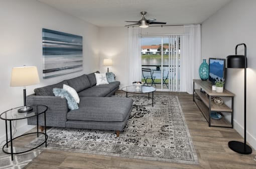A living room with a grey couch, a rug, a table, and a ceiling fan.