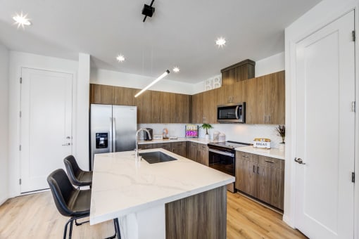 Skye Canyon, NV Apartments Near Las Vegas Strip - Banyan Brighton - Kitchen with Marble Counters, Stainless Steel Appliances, Wood-Inspired Flooring and Cabinets, White Tile Backsplash, and a Large Kitchen Island