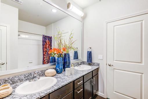 A bathroom with a sink, mirror, and a vase of flowers.