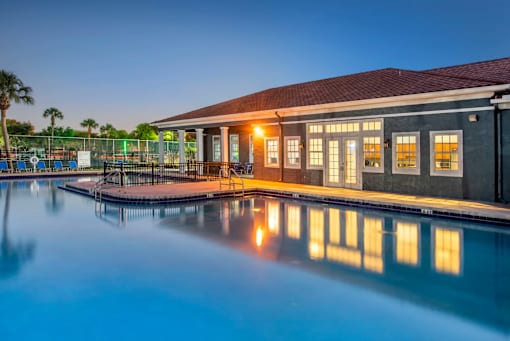 A building with a pool in front of it is lit up at dusk.