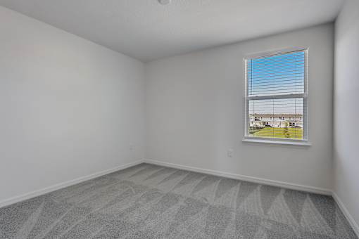 A room with a window and a grey carpet.