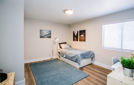 Las Vegas, NV, Apartments Near Best in the West Shopping Center - Haven at Lone Mountain - A Bedroom With White Bed Frame, Blue Bedding, Floor Lamp, Wall Art, And Sliding Closet Doors.
