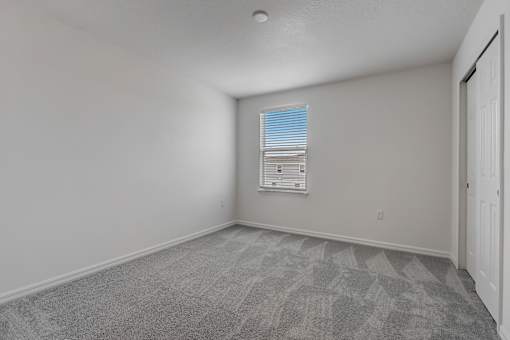 A room with a carpeted floor and a window with blinds.