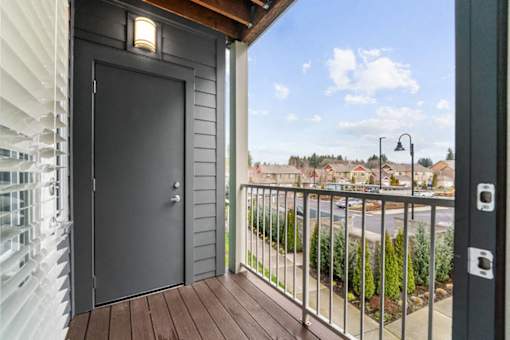 A black door is on the left side of a balcony with a wooden floor.