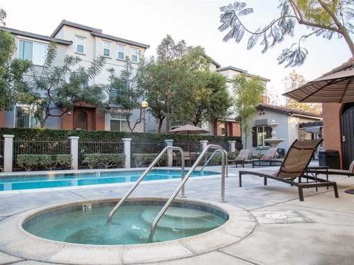 Pet-Friendly Apartments in Tustin, CA - Tustin Cottages - Pool with a Jacuzzi, Trees, and Brown Lounge Chairs