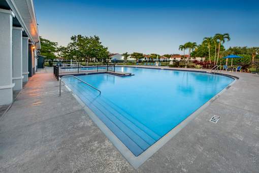 A large outdoor swimming pool with a concrete floor and a metal railing.
