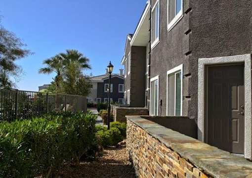 A building with a black door and windows is surrounded by a stone wall and greenery.