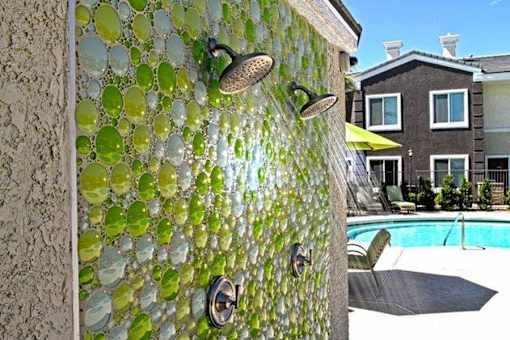 A wall of green glass tiles with a shower head and faucet.