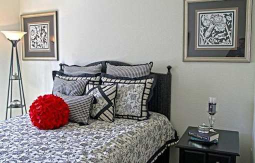 A bed with a red pillow and a lamp on a side table.
