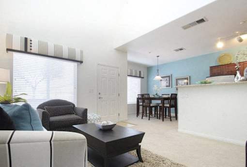 A living room with a white couch, a black coffee table, and a dining area in the background.