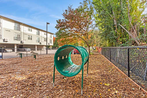 A green playground slide in the middle of a playground surrounded by a fence.
