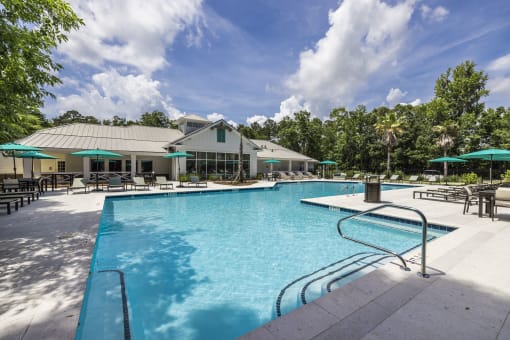 Savannah, GA Apartments – The Palms at Chatham– a large pool with lounge chairs and umbrellas in front of a building