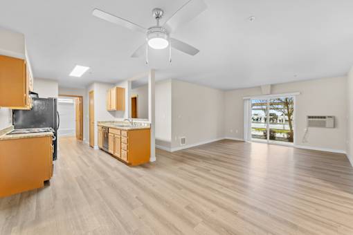 A living room with a ceiling fan and light, hardwood floors, and a kitchenette with a sink and cabinets.
