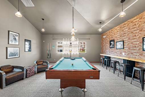 A pool table is in the middle of a room with a brick wall and a bar area.