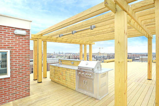 A wooden pergola with a grill on a wooden deck.